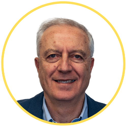 About 5 A man with short gray hair and a light complexion is smiling at the camera. He is wearing a blue jacket and a light blue shirt. The image is framed by a yellow circular border.