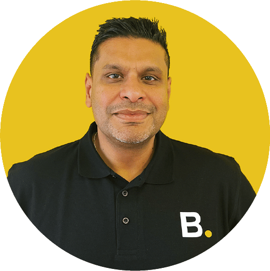 About 3 A man with short hair wearing a black polo shirt with a "B." logo on a yellow background.