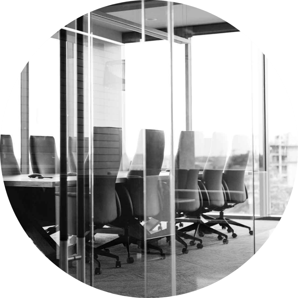 A modern conference room with a long table and several high-back chairs, enclosed by glass walls.