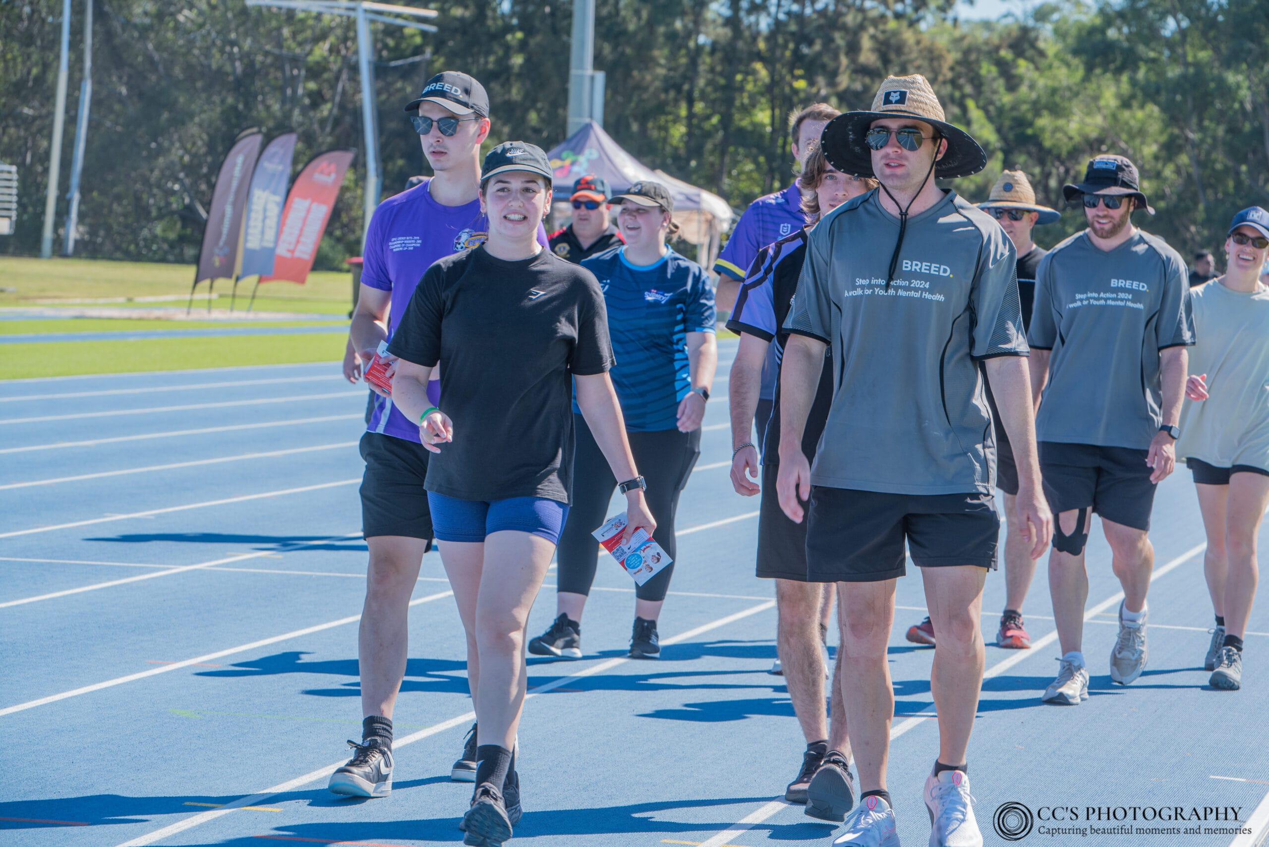 A group of people strides along a blue outdoor track, donning casual sports attire and sunglasses, as part of the vibrant Walk Festival Blacktown.