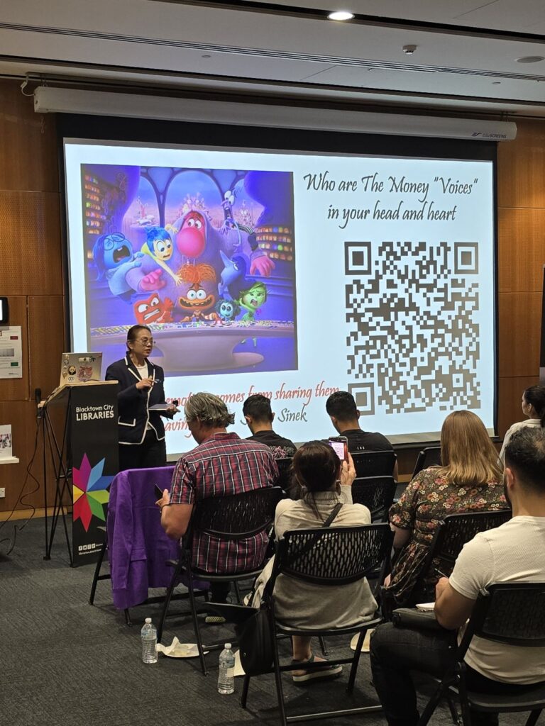 In a cozy library room, a person stands before a slide featuring cartoon characters, a QR code, and the text "Who are The 'Money Voices' in your head and heart," attributed to Simon Sinek. This presentation offers valuable insights for small business owners seeking clarity and inspiration.