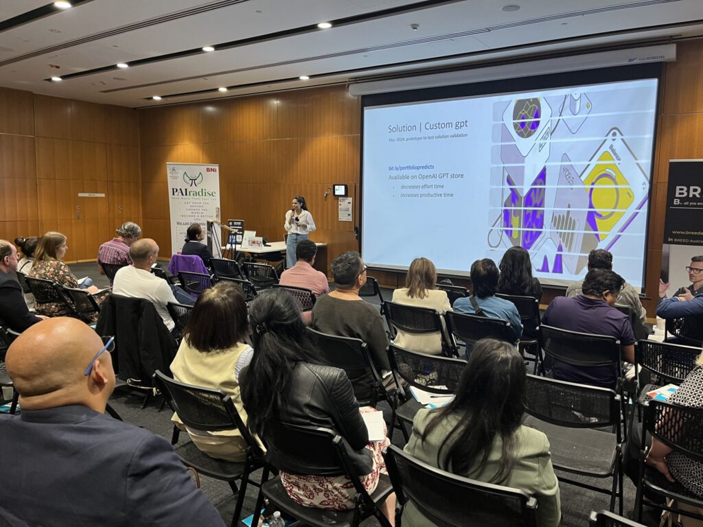 In a conference room, a person presents a slideshow to an attentive audience. The slide highlights a graphic and text about a custom solution tailored for small businesses. Attendees sit facing the presenter, eager to learn how this solution can revolutionize their operations.