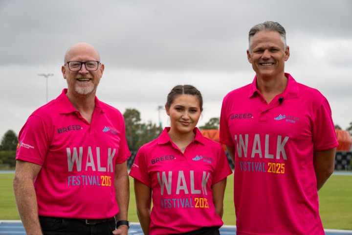 Three people wearing matching pink "WALK FESTIVAL 2023" shirts stand outdoors in Western Sydney, smiling, with a grassy field and overcast sky in the background, celebrating an event supporting youth mental health.