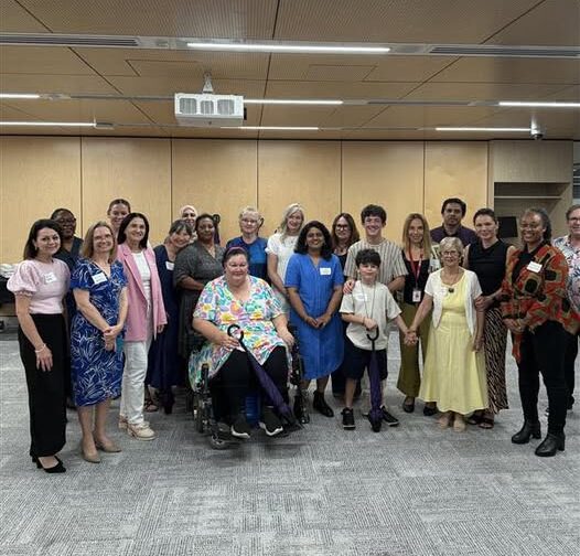 A diverse group of people is gathered for the Beacons of Hope Dinner, with some seated and others standing. They are all smiling warmly at the camera.