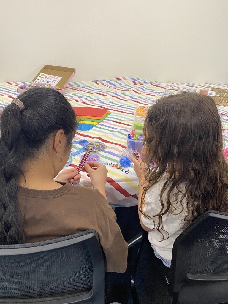 Two girls making loom-band bracelets together at a craft table